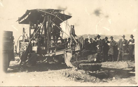 The machine turning the first sod for Parliament House on 29 May 1923. Shows Minister P. Stewart, Joseph Lea in the cab, H.M. Rolland with plans and Colonel Owen behind reporters.