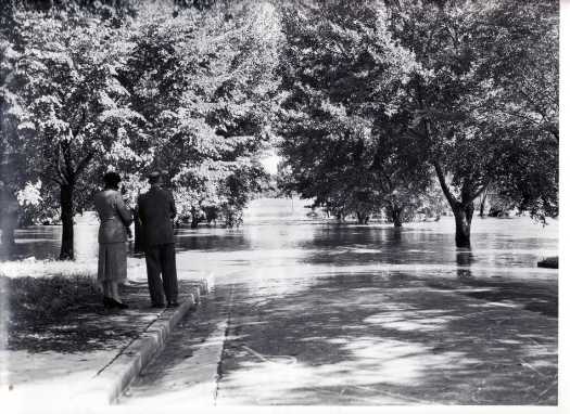 Shows a couple looking at a flooded street at an unknown location.