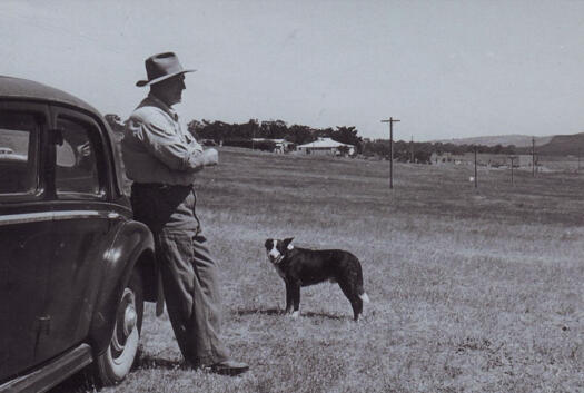 Jack Maguire leaning against his car with his dog nearby and Melrose homestead in the distance