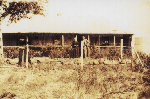 Woman and man standing in front of the first homestead on the site of Kama, now the site of Hawker College