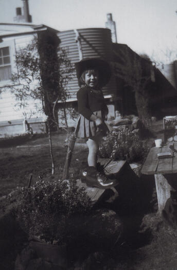 Nan Dixon standing on the seat of a picnic table at Kama wearing her father's boots and slouch hat