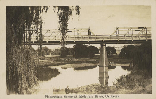 Postcard showing the trestles of the Commonwealth Avenue Bridge over the Molonglo River. A man is standing in the foregound. Flood measure can be seen on one of the bridge piers.