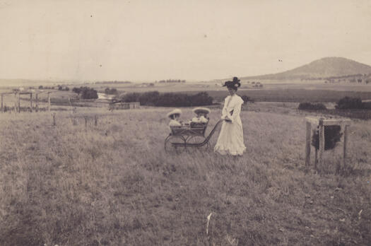 Mrs Kate Rottenberry and two children in a pram, probably on Rottenberry Hill. St John's Church, Mt Ainslie and Scotts farm are visible as is the Molonglo River.