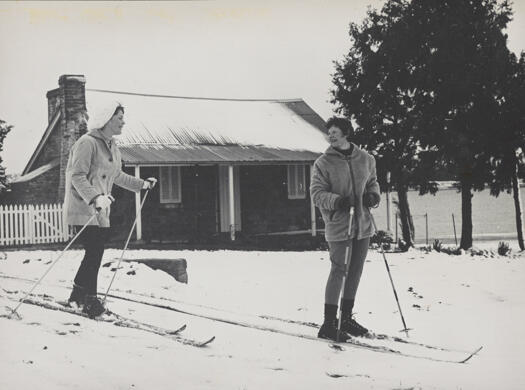 Two women with skis on snow in front of Blundells Cottage