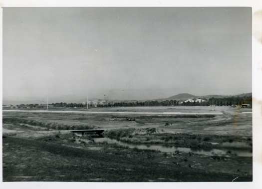 Construction of Lake Burley Griffin from Regatta Point looking west showing Commonwealth Avenue bridge. A temporary crossing over the Molonglo River is visible below Regatta Point.