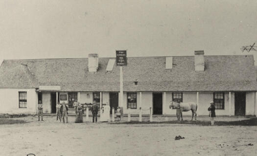 Single storey building. People and horses outside.