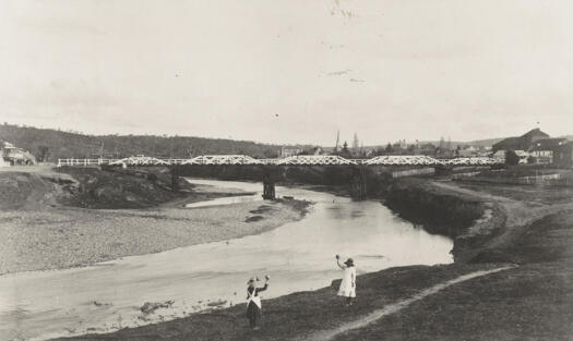 Two girls playing in foreground and the new railway bridge over the river at rear.