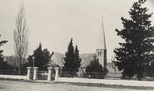 Shows the church and trees and a substantial iron picket fence and gate.