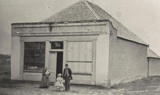 Brick building with steep roof. Single doorway and two large shop windows. Described as a double shop and residence.