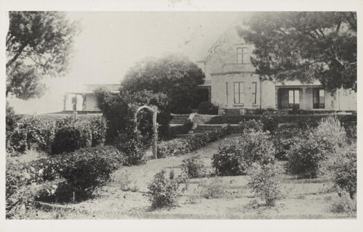 Gardens in foreground and two storey house at rear.