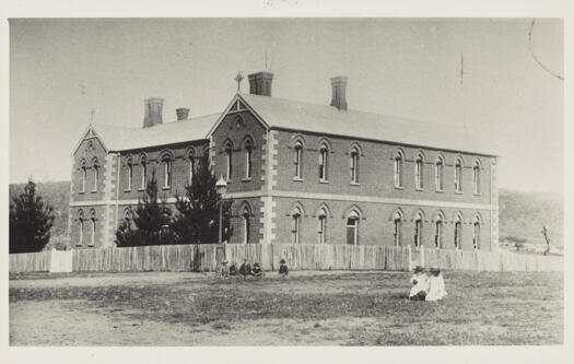 Two storey brick Catholic convent with two groups of children outside.