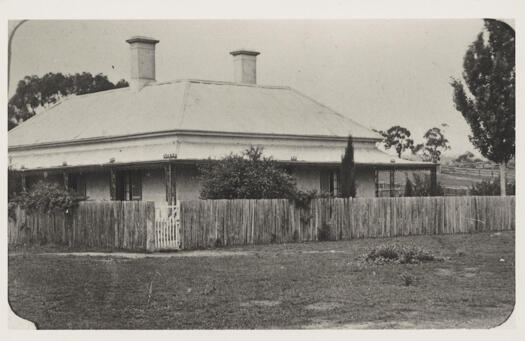 Two chimneys, verandah, on corner with fence. Probably Queanbeyan.